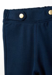 Navyblauwe elastische broek met een gladde textuur, voorzien van een platte tailleband, twee gouden drukknoopjes en zonder zichtbare zakken.