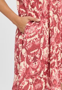 Red and cream patterned fabric with floral motifs, featuring a side pocket, smooth texture, and flowing design.