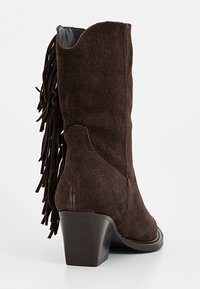 Botín de ante marrón con detalle de flecos en el lado exterior y un tacón grueso, que presenta un forro interior suave.
