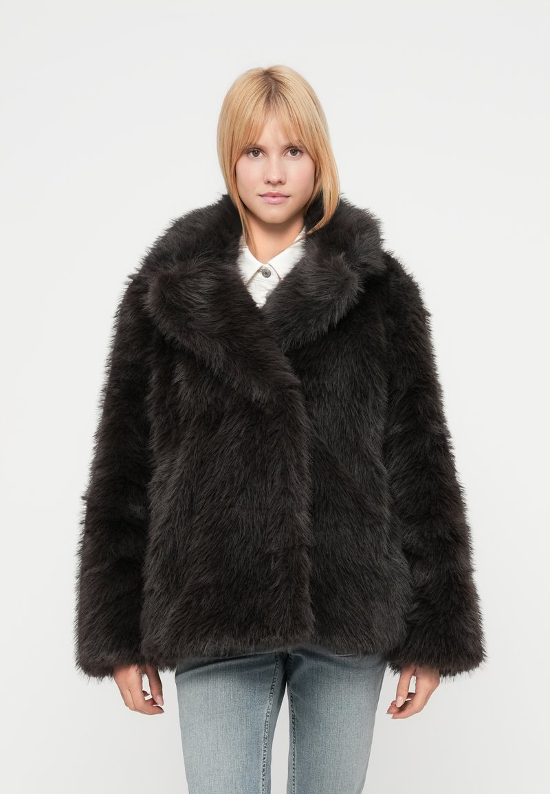 Μαύρο παλτό από συνθετική γούνα με φαρδιά γιακά, μακριά μανίκια και υφή αφράτης, τριχωτής όψης. Η μπροστινή πλευρά είναι διασταυρωμένη με ασύμμετρο σχέδιο.