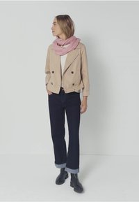 Veste beige croisée, écharpe rose, haut blanc, jeans foncés avec ourlets retroussés et bottines noires. Design simple, texture lisse.