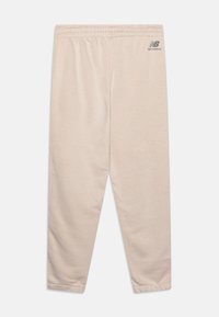 Béžové bavlněné joggery s elastickým pasem, zužujícími se nohavicemi a malým šedým logem na levé přední straně. Hladká textura.