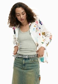 Lillemustriga pikkade varrukatega nööbitav särk, kantud halli tanktopi peal. Sinine teksaseelik, millel on küljetasku ja metallist pandlaga vöö.