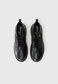 Pantofi din piele neagră cu șireturi, vârful rotunjit, laturi texturate, cu o bucată de prindere la călcâi și talpă din cauciuc. Dispun de șireturi negre și logo pe branț.