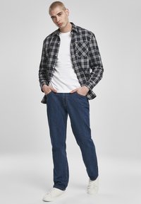 Cămașă din flanel în carouri albastru închis și alb, purtată peste un tricou alb, asortată cu blugi albaștri și adidași albi. Croială casual.