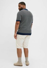 Grå strikket polo-shirt med marineblå krave og mansjetter, parret med cremede shorts. Funktioner inkluderer korte ærmer og tekstureret stof.