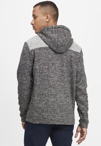 Sudadera con capucha gris y negra de tejido texturizado, con un acento gris claro en los hombros y un diseño de corte relajado.