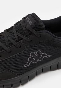 Czarne buty sportowe z siateczkową cholewką, teksturowanymi syntetycznymi akcentami, płaskimi sznurowadłami i gumową podeszwą z charakterystycznym detalem logo.