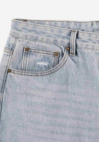 Jasnoniebieskie dżinsy o wysokim stanie, z pięcioma kieszeniami, miedzianymi nitami oraz delikatnymi przetarciami na prawej przedniej kieszeni.