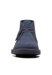 Botas de tobillo de ante azul marino con una textura suave, puntera redondeada, suela plana de goma negra y cordones de contraste en la parte delantera.