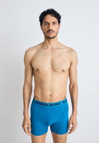 Boxer aderenti da uomo in blu brillante, realizzati in tessuto liscio. Presentano un cinturino elastico nero con il logo "BJÖRN BORG". Design aderente.