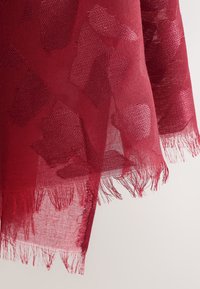 Sheer red scarf featuring a textured pattern of varying shapes, with frayed edges, creating a delicate and lightweight appearance.