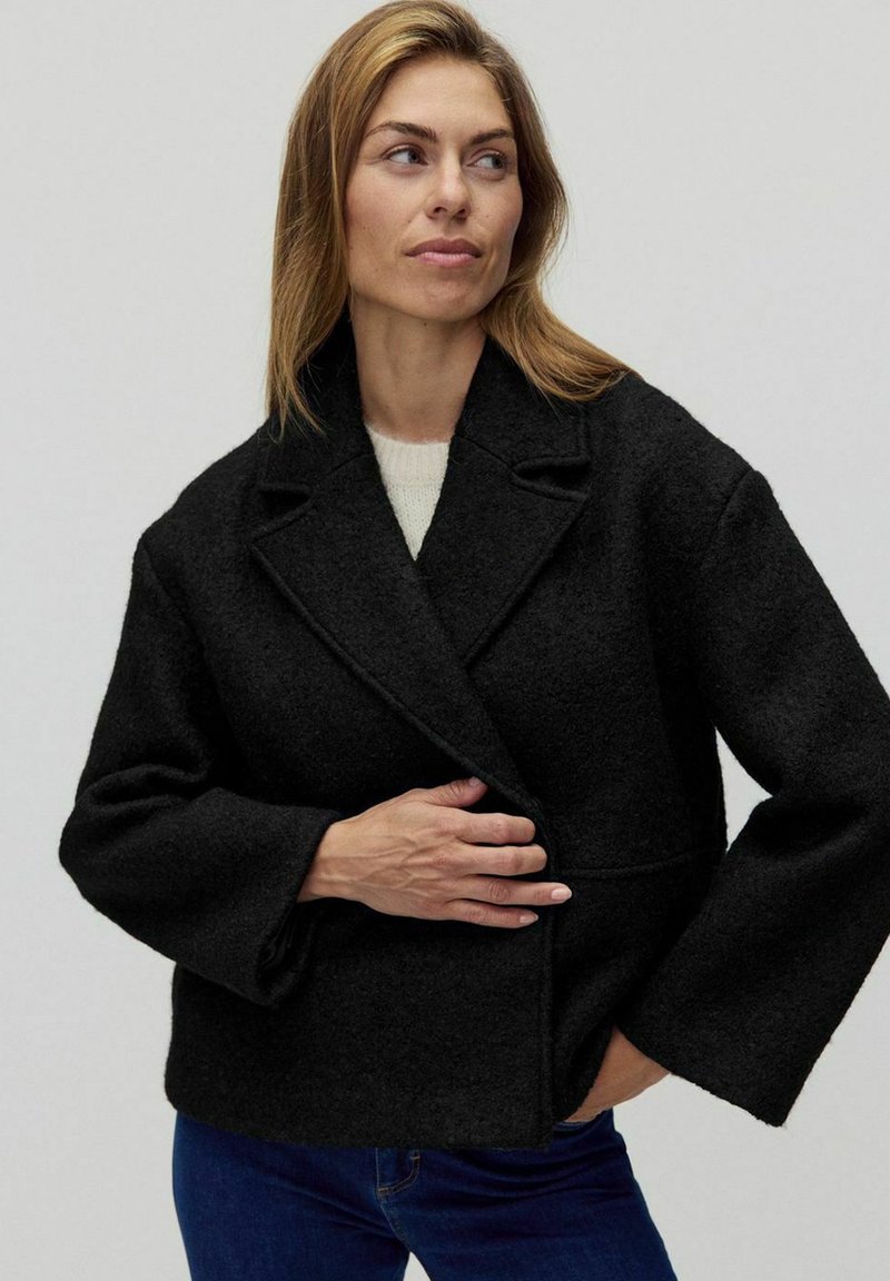 Czarna kurtka z wełny z szerokimi rękawami i zapięciem na dwa guziki. Posiada teksturowany materiał oraz dopasowany krój kołnierza.