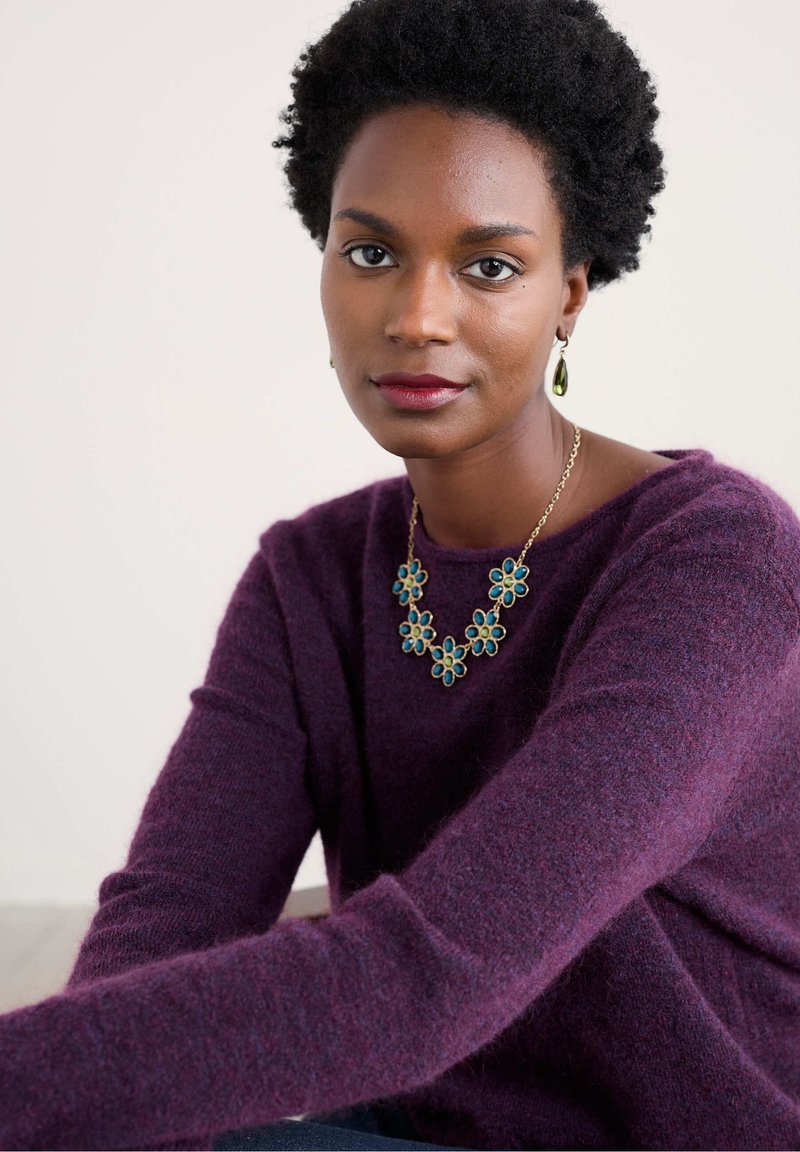 Violeta vilnas džemperis ar garām piedurknēm, kuram ir ziedu kaklarota ar tirkīza akcentiem un atbilstošām auskariem. Gluda tekstūra, brīva piegriezuma.