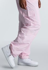 Lichtroze cargobroek van soepel materiaal, met een zijzak en een ontspannen pasvorm, gecombineerd met witte sneakers met een gestructureerde zool.