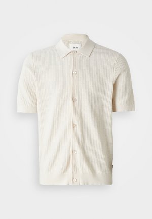 Kortermet, ribbestrikket cardigan i off-white. Har klassisk krage, knappelukking og teksturert stoff. Subtil designdetalj i kanten.
