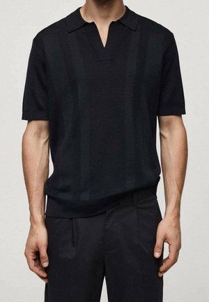 Mann trägt ein schwarzes kurzärmeliges Strick-Poloshirt mit V-förmigem Kragen und schwarze Hose vor hellem Hintergrund.