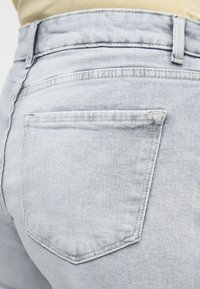 Κοντινό πλάνο στην πίσω τσέπη και τη μέση ενός ανοιχτό μπλε τζιν σε ένα άτομο που φοράει απαλή κίτρινη μπλούζα.