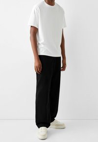 Vit kortärmad t-shirt med rund hals, i kombination med svarta lösa byxor. Avslutas med krämfärgade sneakers. Ren och enkel design.