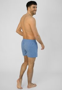Pantaloni da bagno blu da uomo con vita elastica, tessuto testurizzato e vestibilità comoda, mostrati di spalle su un modello con la pelle nuda.