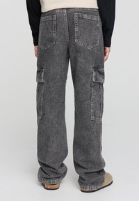 Pantaloni cargo in denim grigio con vestibilità ampia, dotati di doppie tasche laterali, tasche posteriori e una texture sbiadita. Colore solido con cuciture visibili.