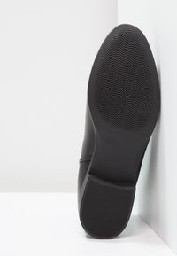 Chaussure noire avec une tige en cuir lisse, un bout rond et une semelle en caoutchouc striée. Affiche la taille 37 sur le dessous.