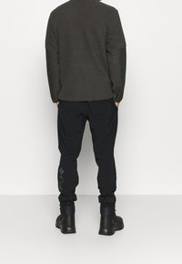 Sweter polarowy w ciemnoszarym kolorze z teksturowanym korpusem i gładkimi rękawami; w połączeniu z czarnymi spodniami z logo i elastycznymi mankietami.