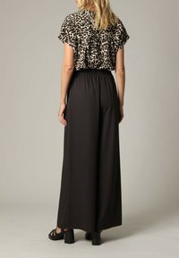 Blouse met luipaardprint en korte mouwen, gecombineerd met losse zwarte broek met elastische tailleband. Zachte textuur, casual pasvorm.