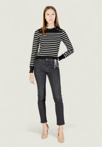 Suéter de rayas en blanco y negro con botones en los hombros, combinado con jeans gris oscuro y tacones nude. Textura suave, diseño ajustado.