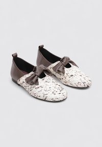 Chaussures plates avec un motif tacheté blanc et marron, des accents en cuir marron et un détail de nœud à l'avant. Bout et arrière arrondis.