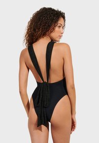 Crni jednodijelni kupaći kostim s niskim leđima, s dugim, teksturiranim trakama vezanim u struku. Visoko izrezana otvora za noge i glatkasti završetak.