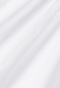 Bílá tkanina s hladkou, matnou strukturou, vykazující jemné vrásky a záhyby, což naznačuje lehkost a vzdušnost.