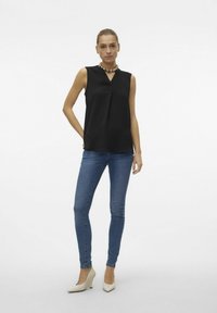 Haut sans manches noir avec un décolleté en V et une texture subtile, associé à un jean skinny bleu et des talons aiguilles blancs.