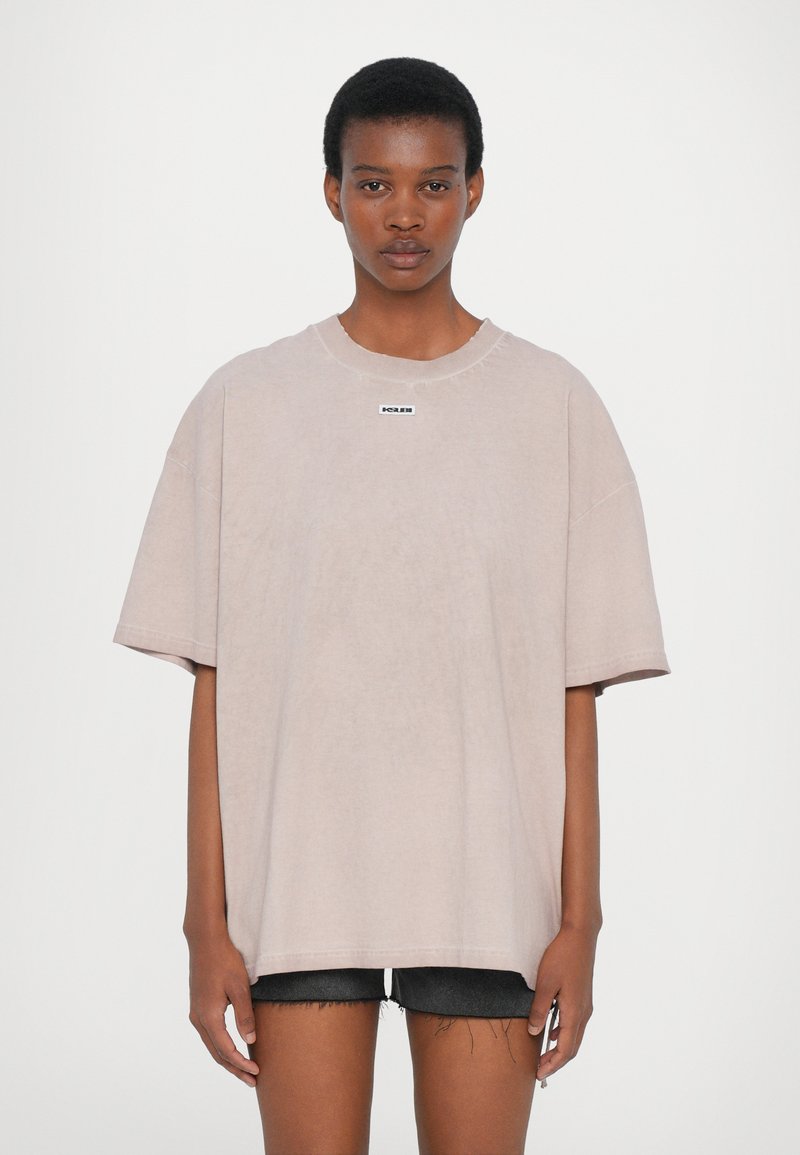 Light pink oversized t-shirt made of cotton, featuring a round neckline, dropped shoulders, and a small black logo on the chest.