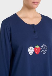Maglietta a maniche lunghe blu navy con scollo rotondo e due bottoni neri. Presenta tre grafiche di fragole in bianco, rosso e verde. Texture liscia.