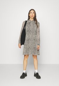 Vestido de manga longa com estampa animal em bege e preto, com gola e saia evasê; combinado com uma bolsa tote preta e sapatos pretos de solado grosso.