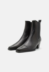 Botines de cuero negro con punta puntiaguda, paneles elásticos laterales y tacón estrecho. Textura suave con un diseño minimalista.