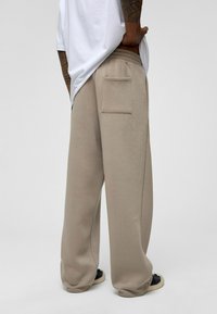 Beige wijde sweatpants van zachte stof, met een achterzak en een elastische tailleband, gecombineerd met een losse witte t-shirt.