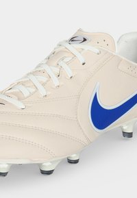 Σοσονάκι ποδοσφαίρου Nike εκρού με γαλάζιο λογότυπο swoosh, λευκά κορδόνια και λευκές μύτες με μαύρες άκρες στη σόλα.