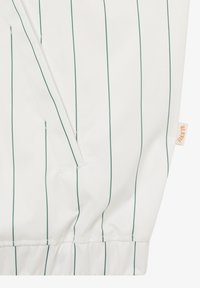 Biały materiał z cienkimi pionowymi zielonymi prążkami, szew z elastycznym wykończeniem na dole oraz mała beżowa metka po boku.