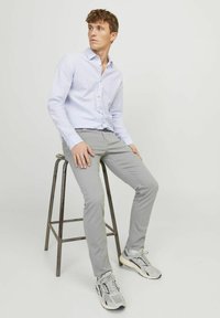 Světle modrá pruhovaná košile s knoflíky, šedé chinos kalhoty a šedé tenisky. Košile má špičatý límec a chinos mají úzký střih.