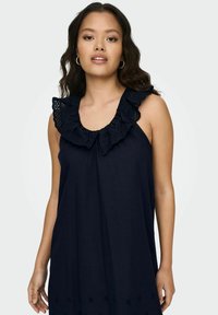 Robe sans manches bleu marine avec un col à volants agrémenté de dentelle et d'une broderie florale sur l'ourlet. Fabriquée en tissu léger, coupe décontractée.
