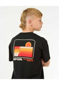 T-shirt en coton noir avec un graphique rétro coloré au dos représentant un soleil et des collines superposées. Le texte comprend "RIPCURL" et "Produits de surf de qualité."