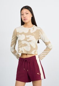 Haut court à manches longues beige avec un motif abstrait de tigre marron clair ; associé à un short bordeaux avec des rayures blanches sur les côtés et des accents dorés.