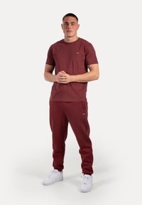 Bordeaux T-shirt og matchende joggers, lavet af bomuld, parret med hvide sneakers. Simple design med minimal branding på stoffet.