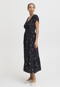 Robe maxi noire à motifs floraux avec manches bouffantes courtes, corsage smocké, ourlet à volants en plusieurs niveaux et motifs de fleurs multicolores partout.