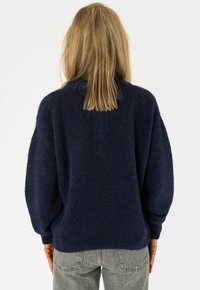Maglione oversize blu navy con finitura morbida e testurizzata, spalle leggermente abbassate e polsini a coste. Indossato con jeans grigio chiaro.