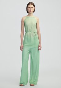 Top verde, tessuto testurizzato, senza maniche con vita legata abbinato a pantaloni a gamba larga, entrambi con un motivo sottile e materiale leggero.