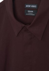 Camisa de mezcla de algodón burdeos con un collar flexible, corte regular y etiquetas de detalle en el cuello interior, enfatizando su textura suave.