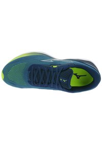 Zapatilla deportiva azul con parte superior de malla, diseño texturizado, acentos verdes y cordones planos. Presenta una suela suave y acolchada, además de un detalle con el logo.